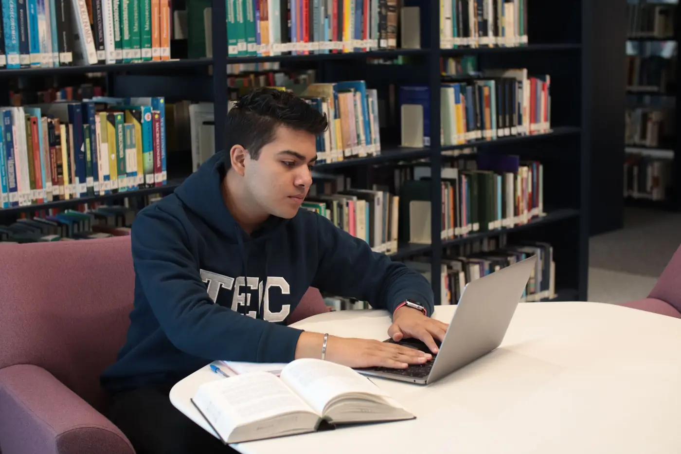 A student studying in a library with a laptop and textbooks